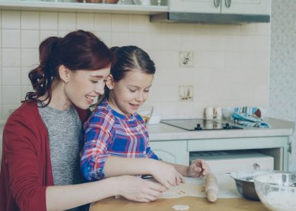 Smiling mother and cute daughter making Christmas cookies together sitting at modern kitchen at home. Family, food and people concept