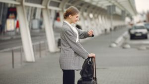 Side view of happy woman in checkered jacket standing with luggage and looking on watch before flight departure in airport